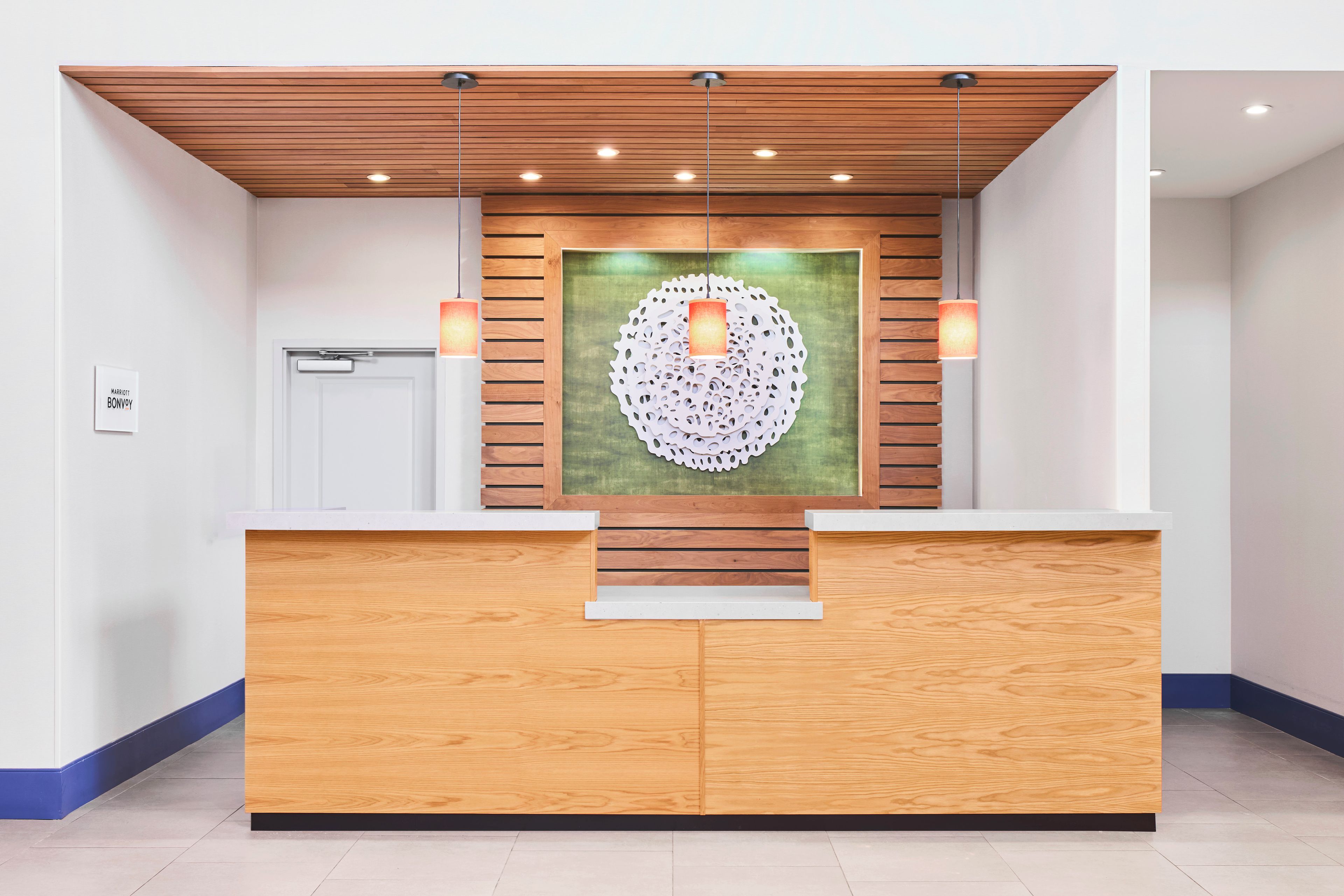 A reception desk with a wooden finish, a green-framed artwork, and two wall-mounted lamps.
