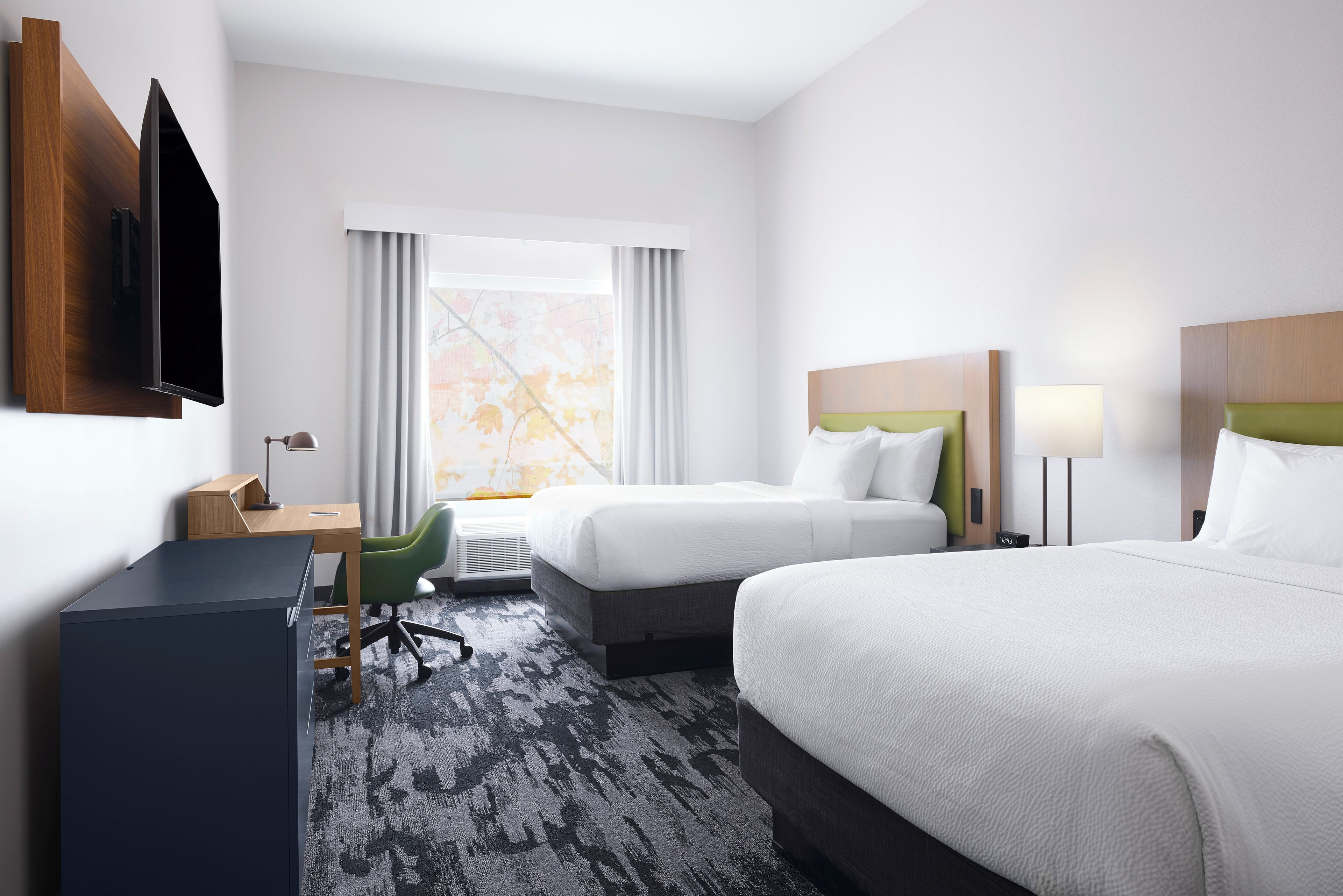 A hotel room with two beds, a desk, a chair, a TV, and a window with curtains.