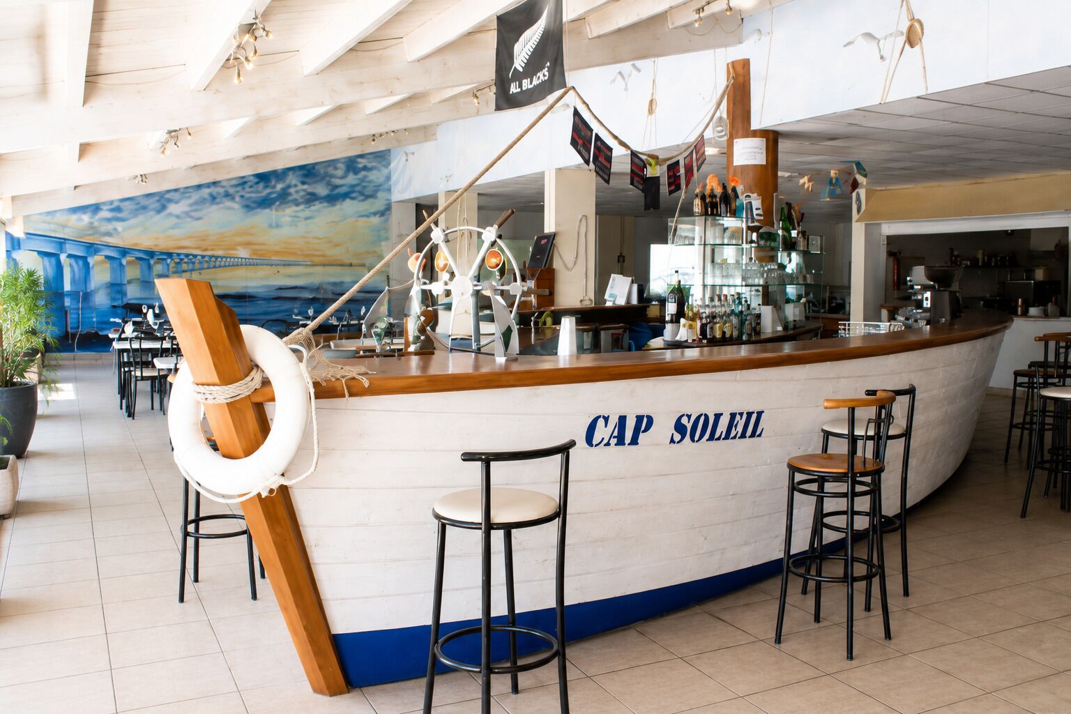 Un bar appelé « CAP SOLEIL », décoré sur le thème de la marine, avec notamment une bouée de sauvetage et un gouvernail de navire.