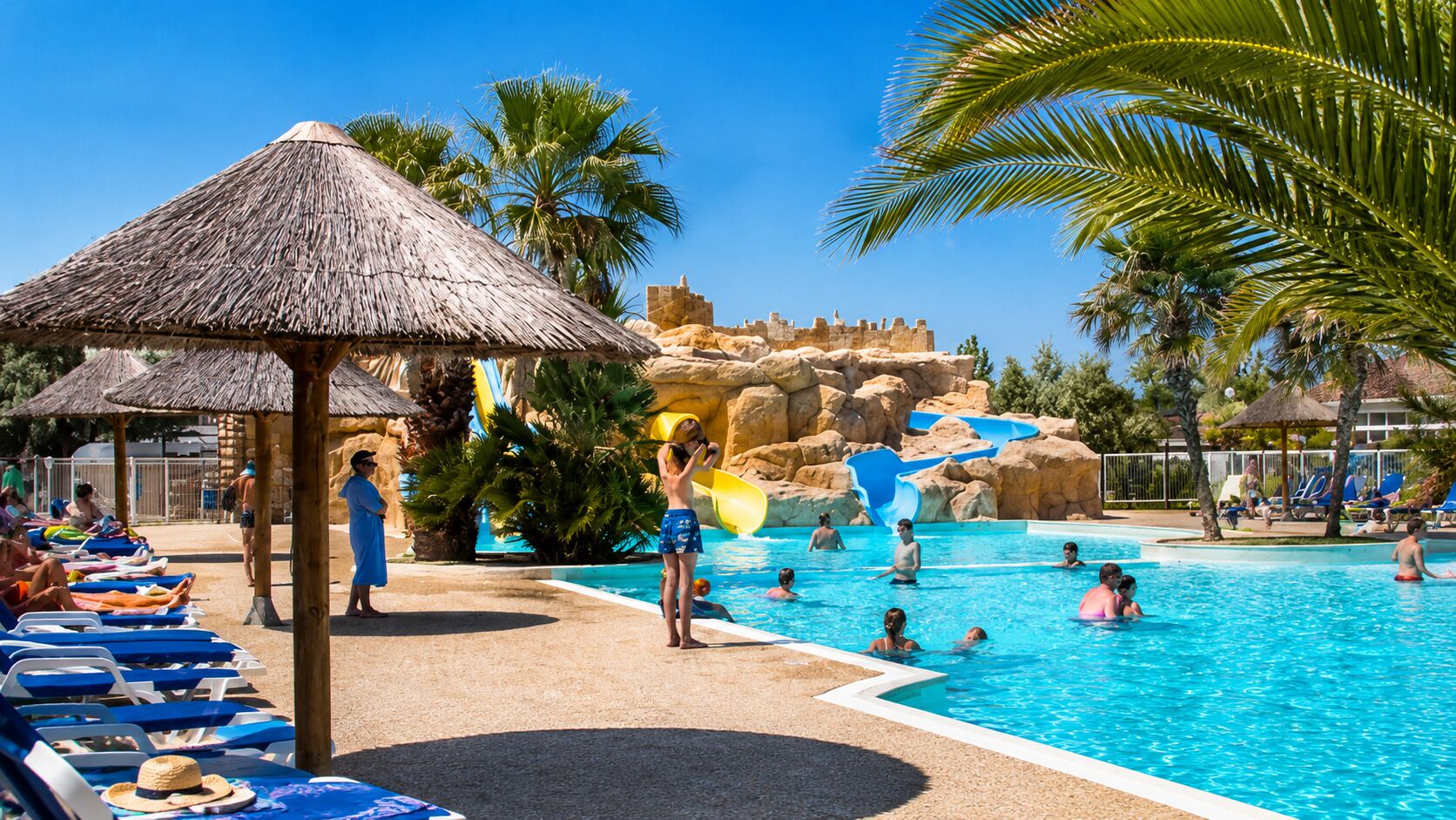 A swimming pool with a water slide, lounge chairs, and palm trees.