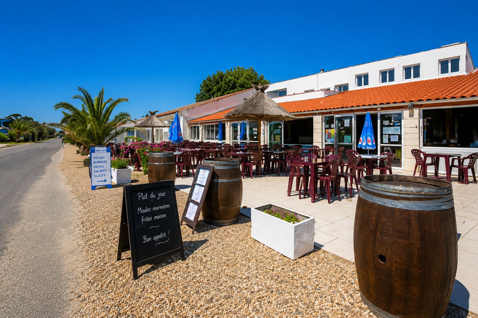An outdoor dining area with tables and chairs, wooden barrels, and a chalkboard menu.