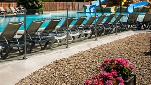 Zona de piscina amb gandules, tobogan aquàtic, palmeres i un cel blau i clar.