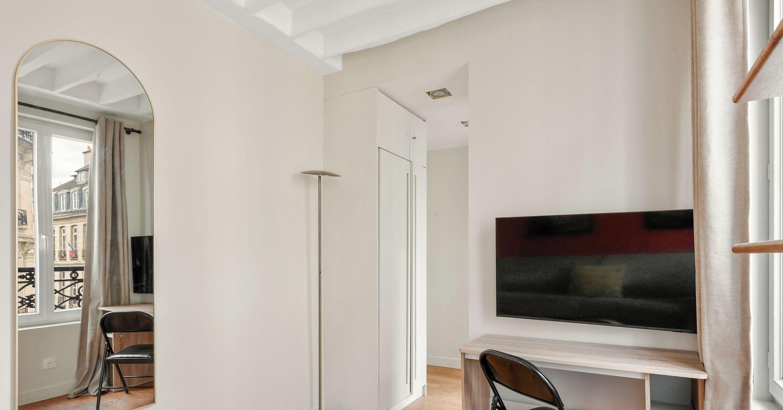Uma sala de estar moderna com televisão de tela plana, uma área de jantar com uma cadeira e vista para um edifício por um arco.