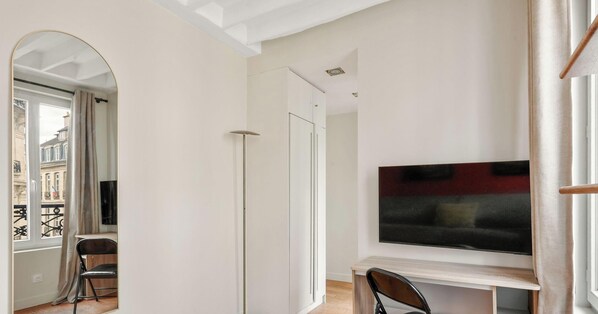 Una sala moderna con televisor de pantalla plana, un comedor con una silla y vistas a un edificio a través de un arco.