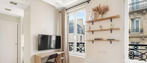 Un salon moderne doté d’un téléviseur à écran plat, de meubles en bois, d’objets décoratifs disposés sur des étagères et offrant une vue sur la ville grâce à de grandes fenêtres.