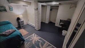 Een kamer met een bed, nachtkastje, lamp, wandplank en een deur naar een andere kamer.