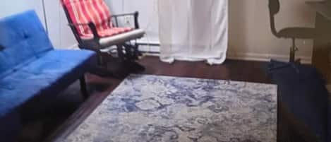 Un salon avec un canapé bleu, un fauteuil à rayures rouges et noires, un tapis à motifs et une lampe.