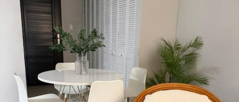 A dining area with a round table, white chairs, and a wicker chair.