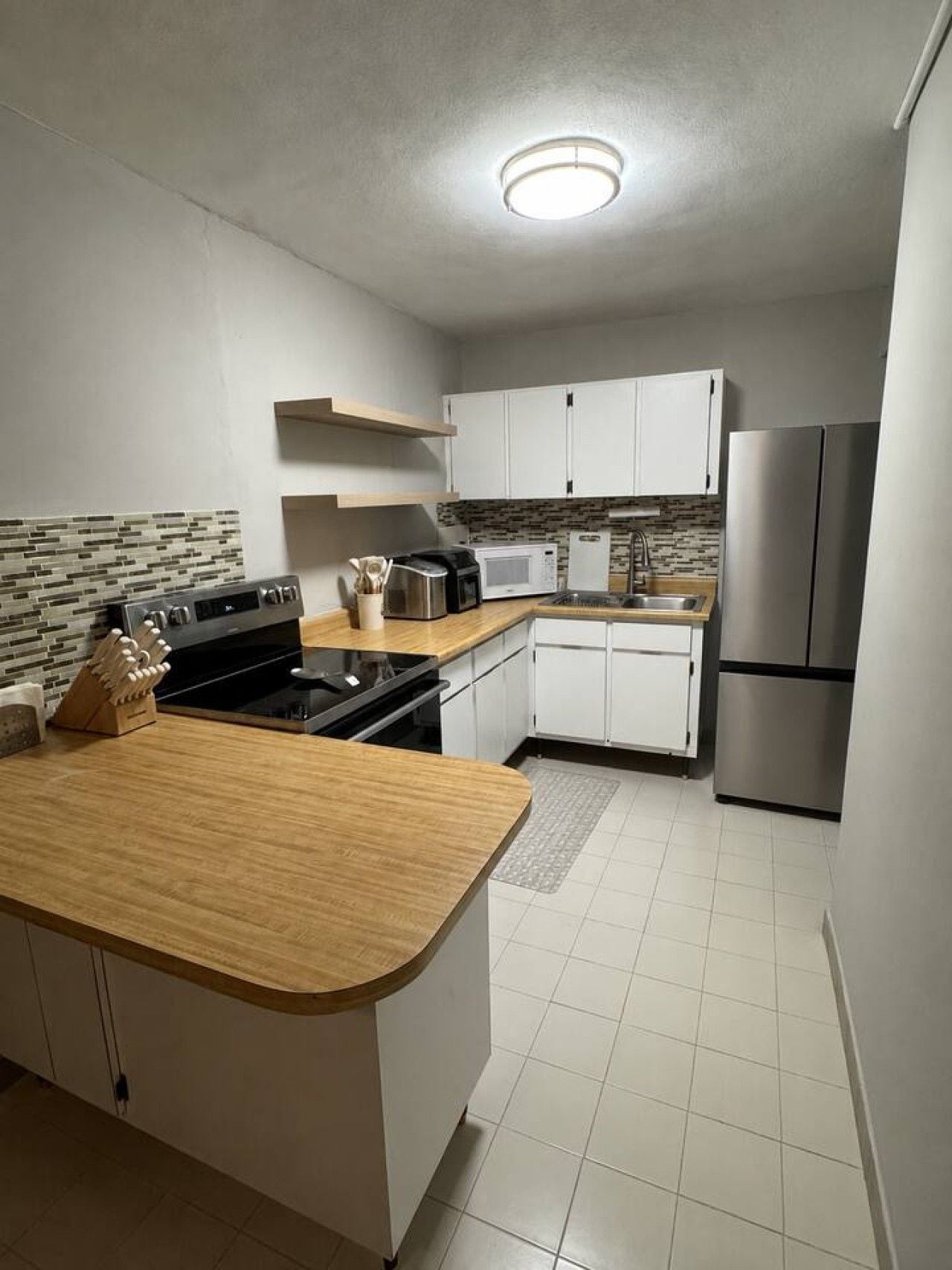 A compact kitchen with white cabinets, a stainless steel refrigerator, a microwave, and a stove.