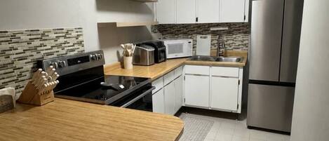 A compact kitchen with white cabinets, a stainless steel refrigerator, a microwave, and a stove.