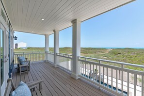 A covered outdoor area with a wooden deck, white railings, and a view of the beach and ocean. - Luxurious Retreat. Ocean Views. Steps to the Beach (Port Aransas)