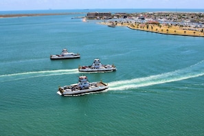 Three large boats on a calm sea with a coastal cityscape in the background.