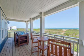 A covered outdoor area with a table and chairs, overlooking a coastal landscape. - Blue Haven Retreat – Coastal Luxury Steps to Beach (Port Aransas)