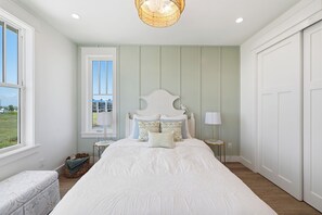 A bedroom with a large bed, a window with a view, a bedside table with a lamp, and a door. - Luxurious Retreat. Ocean Views. Steps to the Beach (Port Aransas)