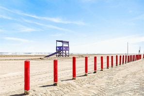 A lifeguard tower on a sandy beach with red posts lining the shore.