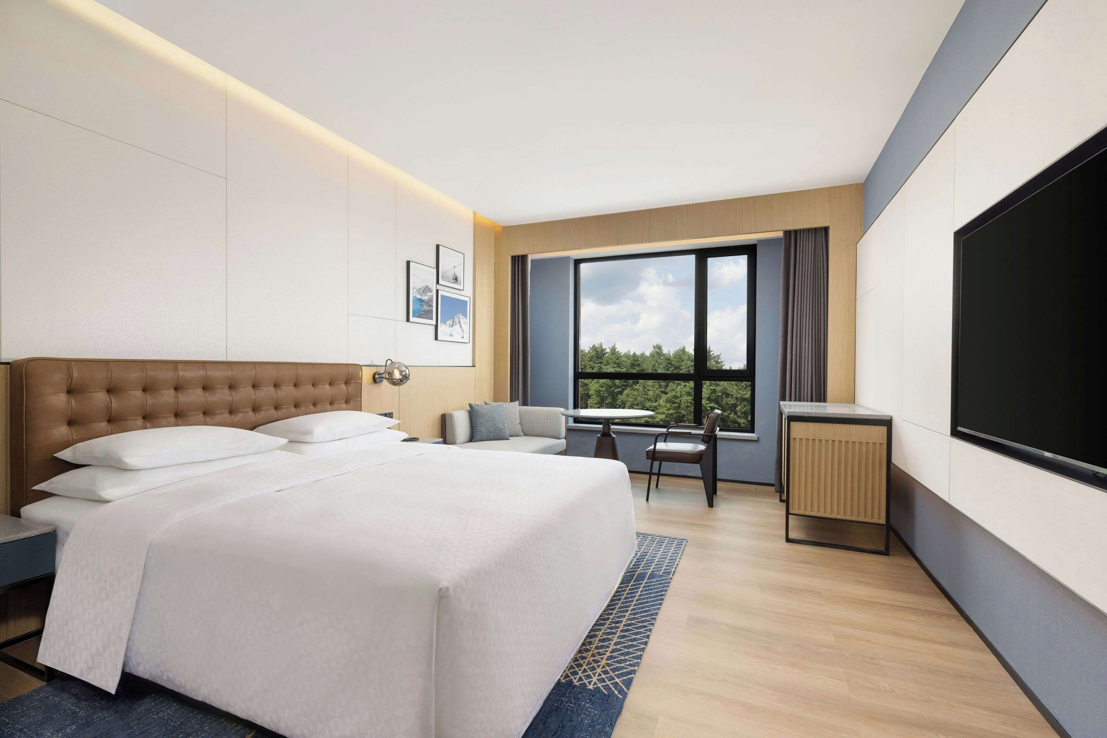 A modern hotel room with a large bed, a desk, a chair, and a TV.