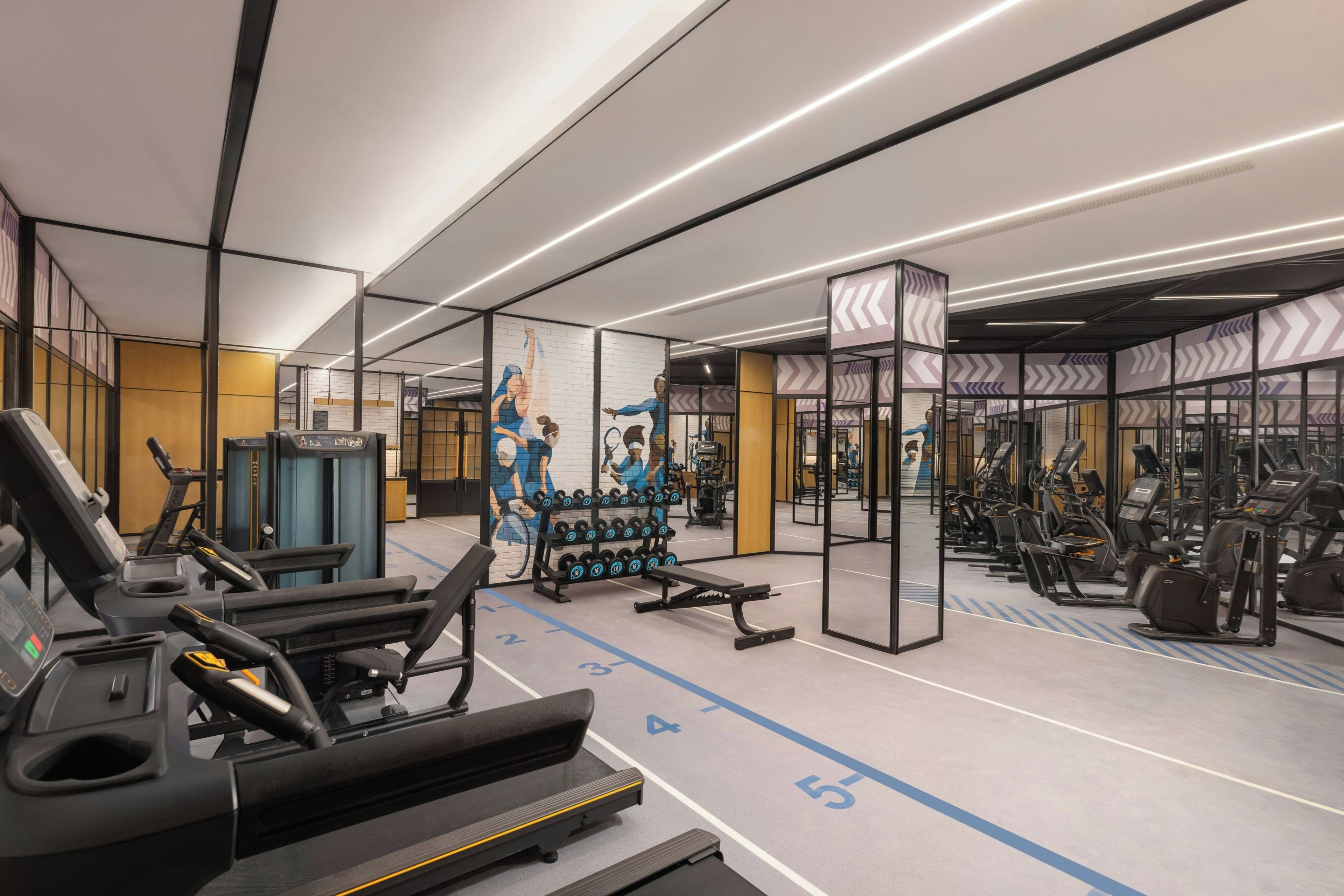 Een moderne sportschool met loopbanden, krachtapparaten en een spiegelwand.