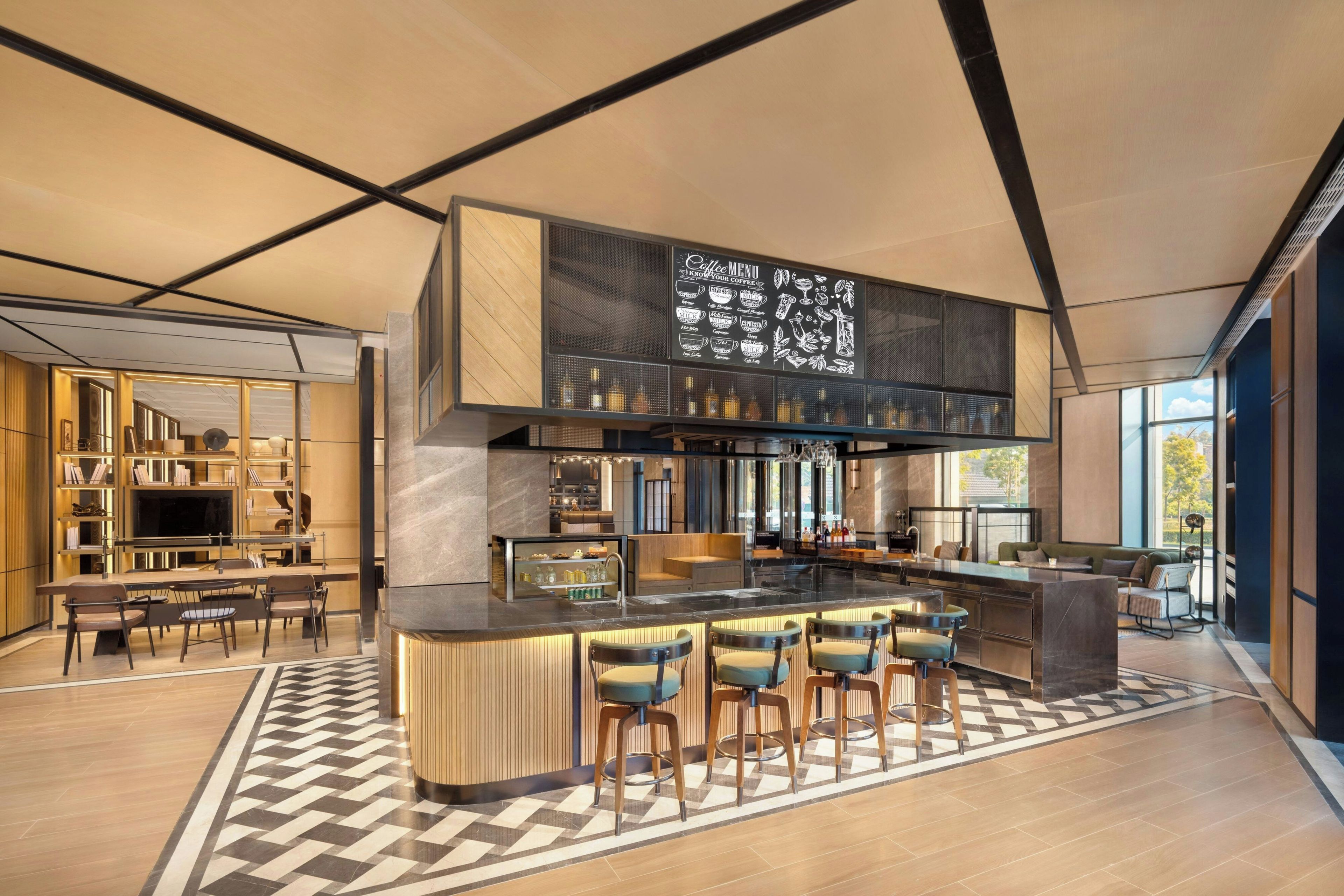 A modern bar area with a coffee menu display, bar stools, and a seating area with a patterned floor.