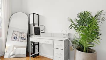 A white desk with drawers, a large mirror, and a potted plant.