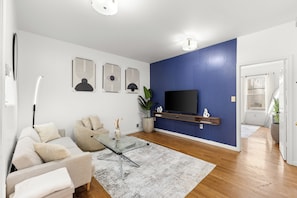 Een woonkamer met een bank, een glazen salontafel, een televisie op een dressoir en een blauwe accentmuur.