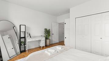 A bedroom with a bed, a desk, a mirror, a potted plant, and white doors.