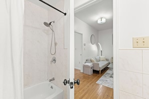 Een moderne badkamer met een douche, een bad en een toilet. De ruimte heeft witte wanden en een houten vloer.