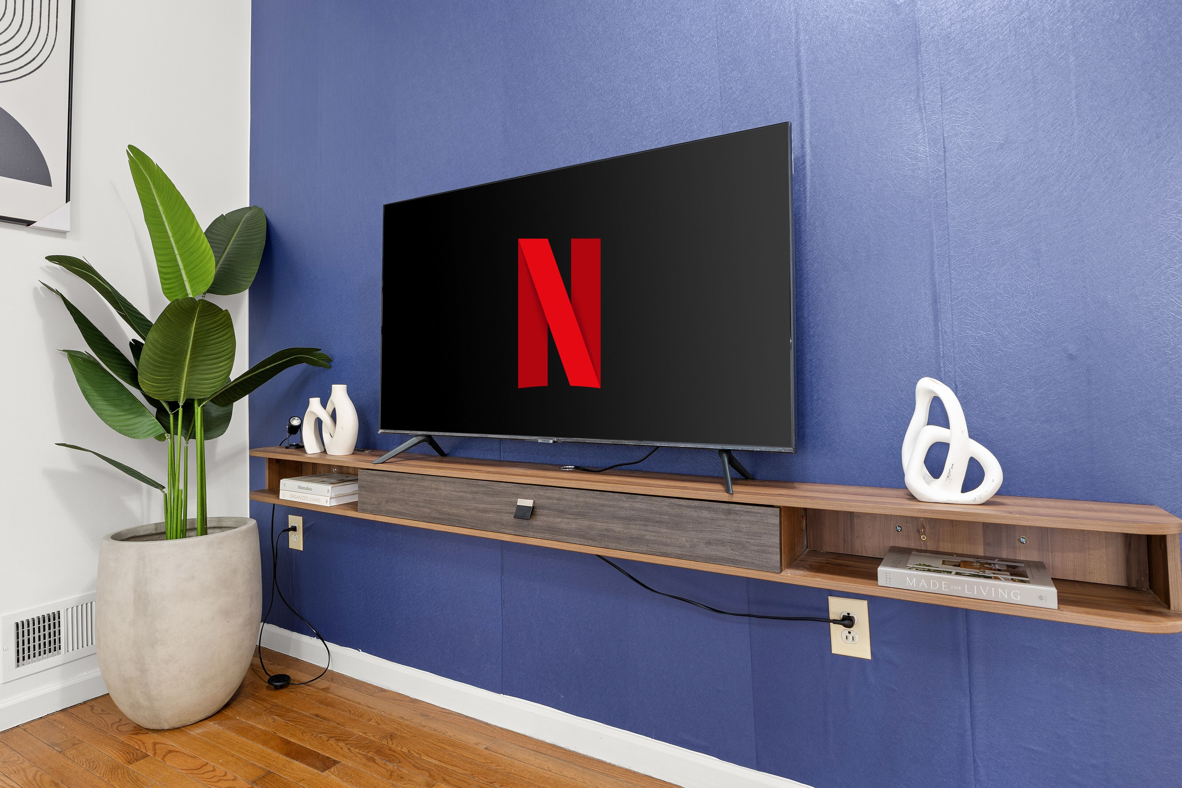 A flat-screen TV mounted on a blue wall with a wooden shelf below.
