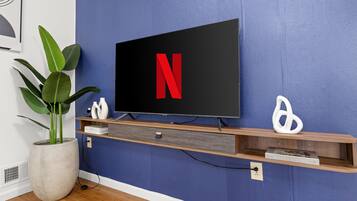 A flat-screen TV mounted on a blue wall with a wooden shelf below.