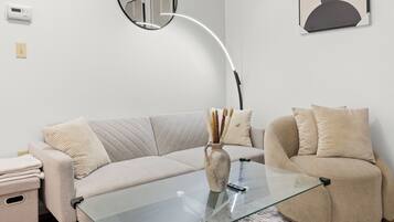 A modern living room with a glass coffee table, beige sofas, a vase with dried plants, and a wall-mounted mirror.