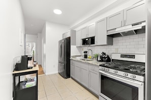 Een moderne keuken met grijze kastjes, een zwarte koelkast, een magnetron, een gasfornuis en een koffiezetapparaat op een houten plank.