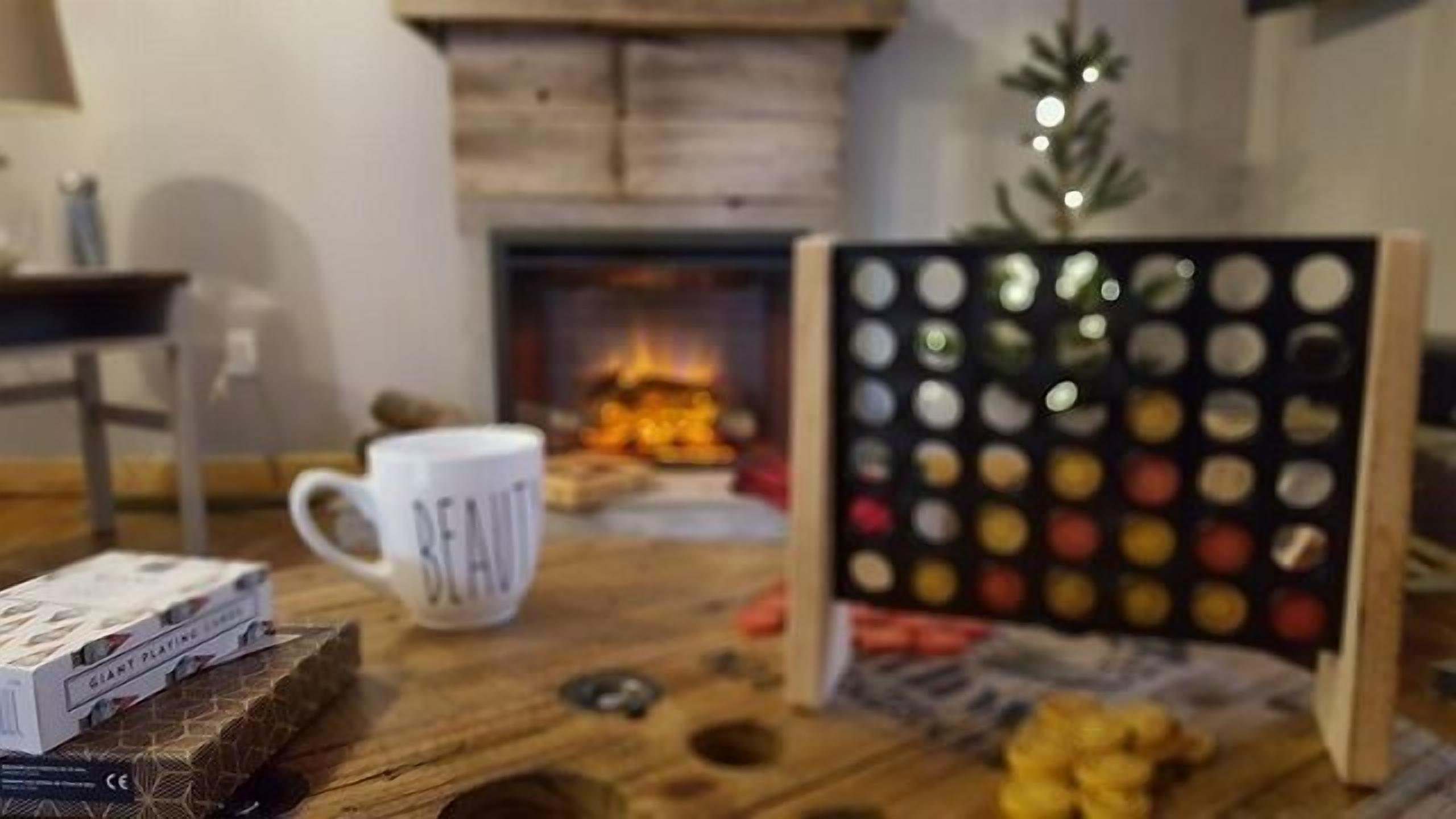 A cozy room with a fireplace, a small Christmas tree, and a board game.