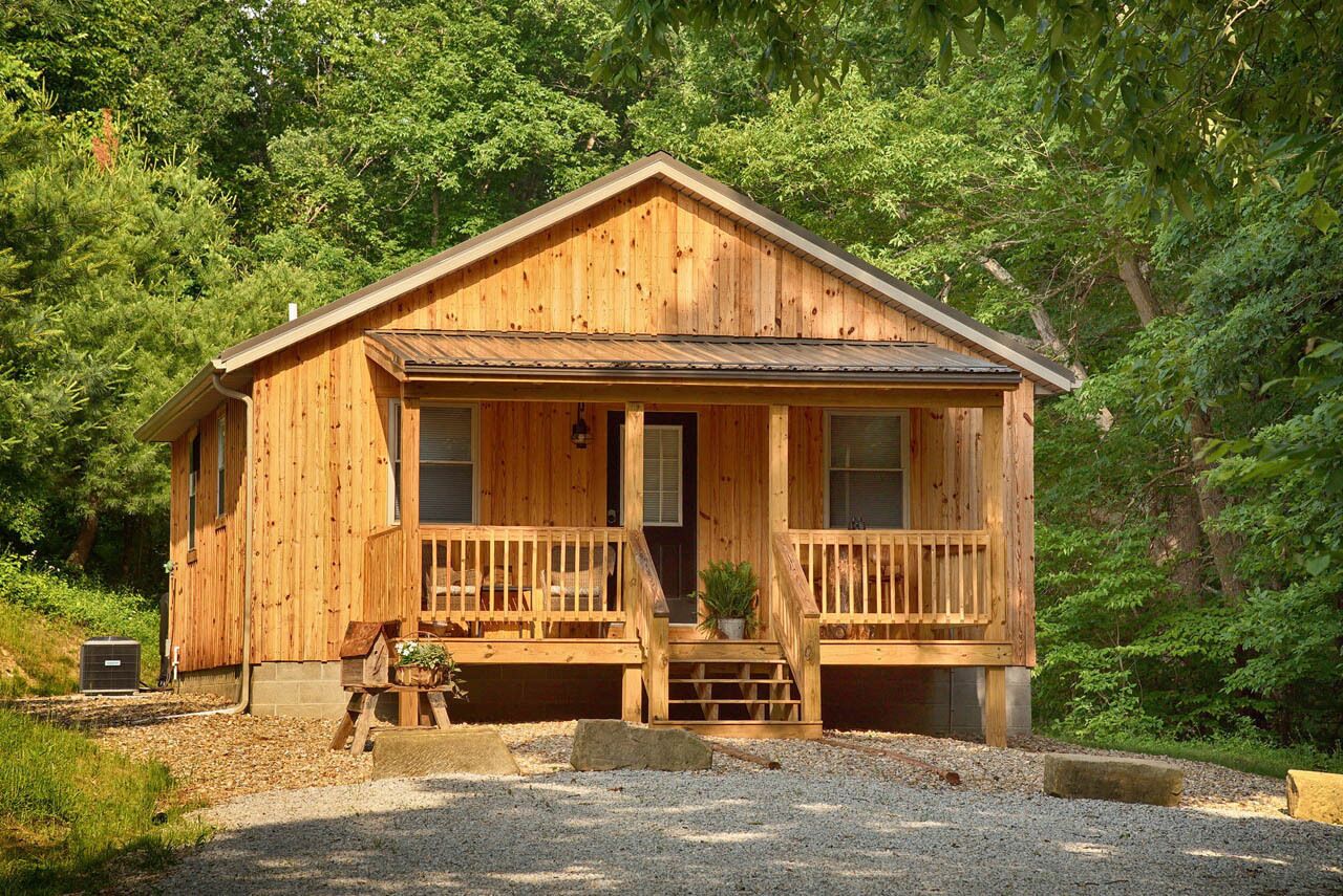 A wooden cabin with a porch, a front door, and a small front yard.