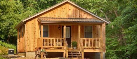 A wooden cabin with a porch, a front door, and a small front yard.