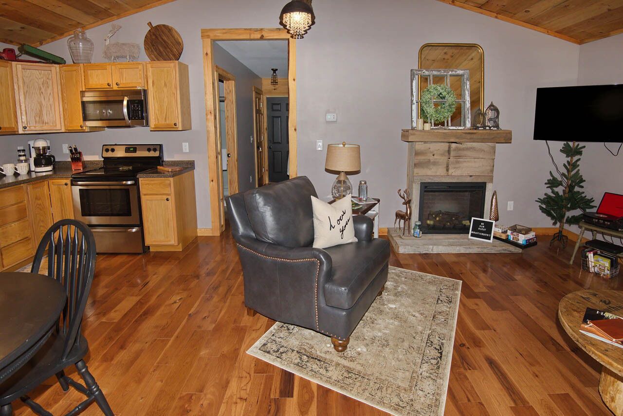 A cozy living room with a fireplace, a leather sofa, a dining table with chairs, wooden cabinets, and a kitchen area with appliances.