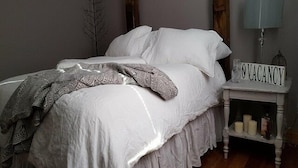 A bed with a white comforter and a patterned throw blanket, a bedside table with a 'VACANCY' sign, and a lamp. - Rustic Roots Cabin - Adults Only (Logan)
