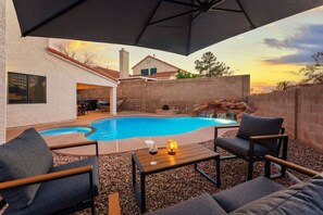 Un área de piscina al aire libre con terraza, asientos y una cascada.