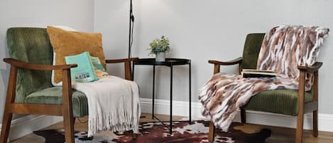 A room with two green upholstered chairs, a small table, a cowhide rug, and a floor lamp.