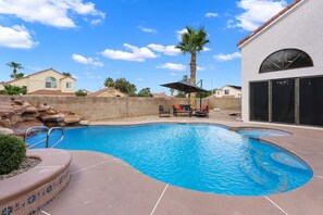 A swimming pool with a stone wall, lounge chairs, and a palm tree. - Pool + Hot Tub l Game Room l 20 Min to the Strip (Henderson)