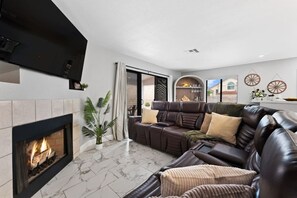 Una sala de estar moderna con chimenea, sofá de cuero y un ventanal grande.