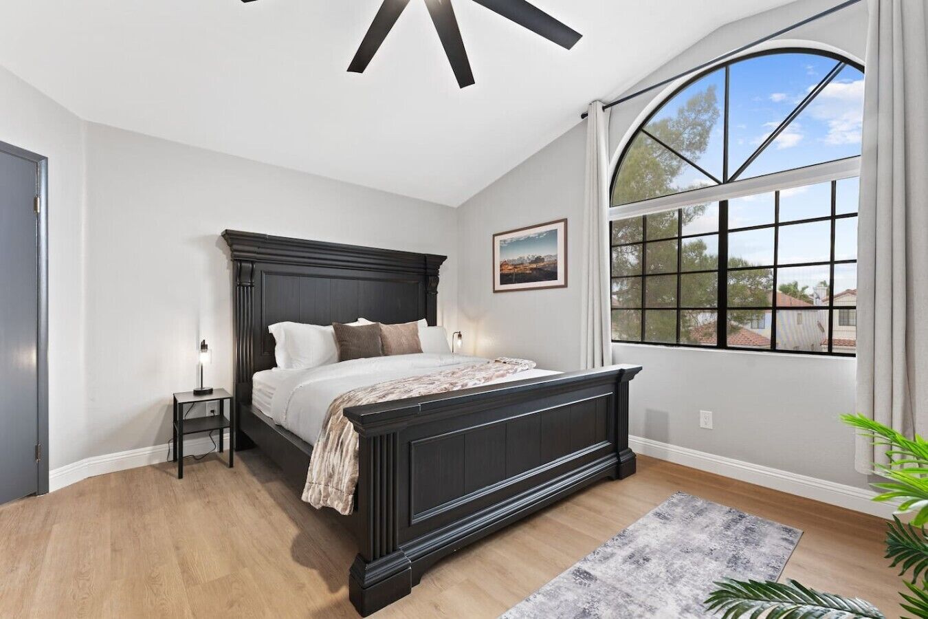 Une chambre avec un grand lit, une table de chevet, une fenêtre donnant sur un beau paysage et un ventilateur de plafond.