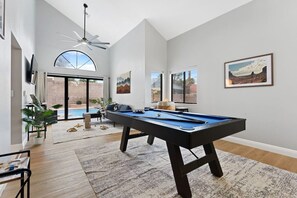 A pool table in a room with a large window, a ceiling fan, and a view of a swimming pool. - Pool + Hot Tub l Game Room l 20 Min to the Strip (Henderson)