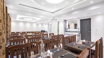 A hotel dining area with multiple tables, chairs, and a modern ceiling design.