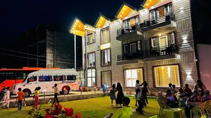 A multi-story building with balconies, a bus parked in front, and people gathered outside. - Hotel Classy Castle (Pahalgam)