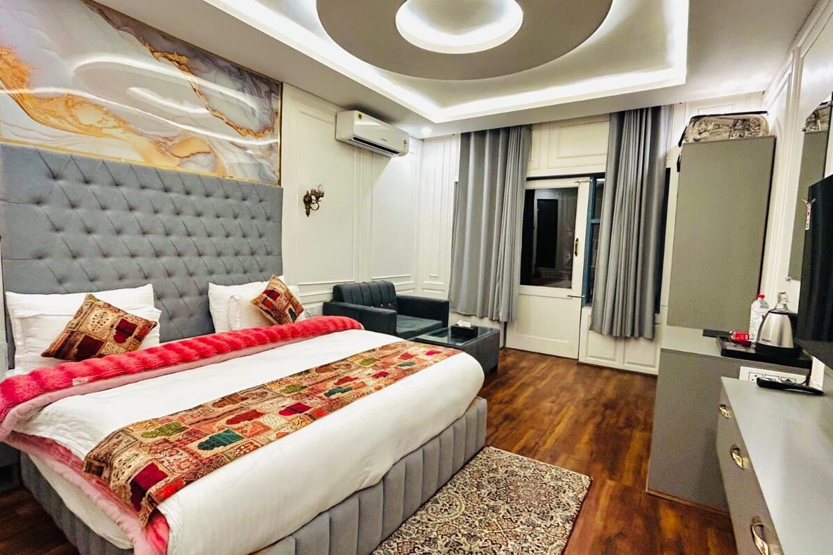 A hotel room with a large bed, a desk, a chair, an air conditioning unit, and a television.