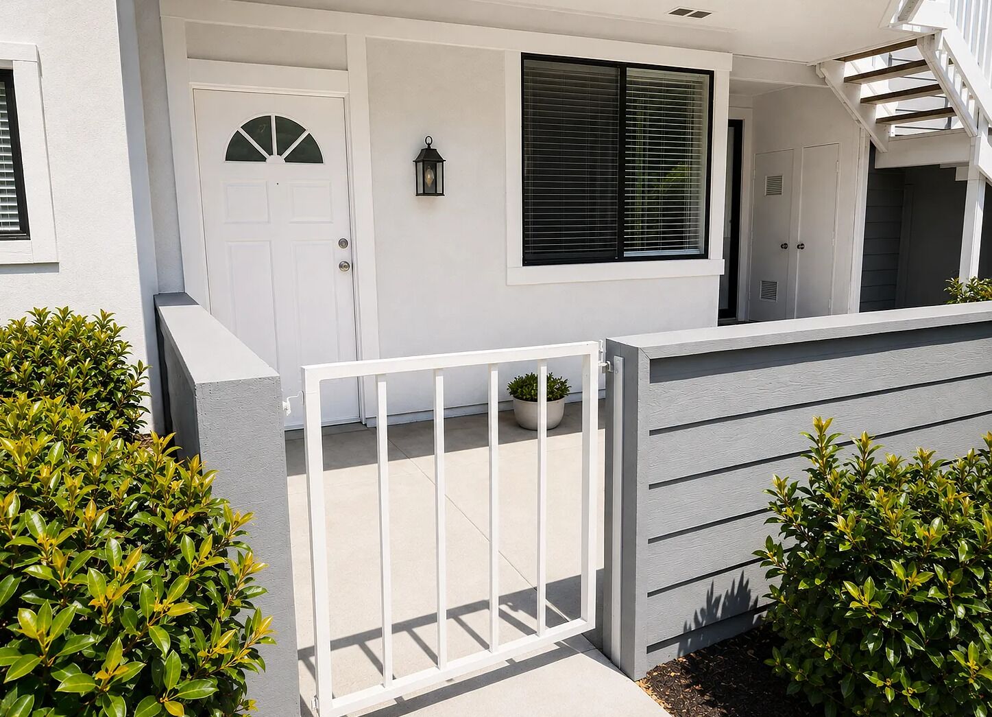A modern residential building with a white exterior, a gated entrance, and a potted plant near the door.