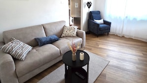 Un salon avec un canapé, une table basse, un fauteuil et un tableau accroché au mur.