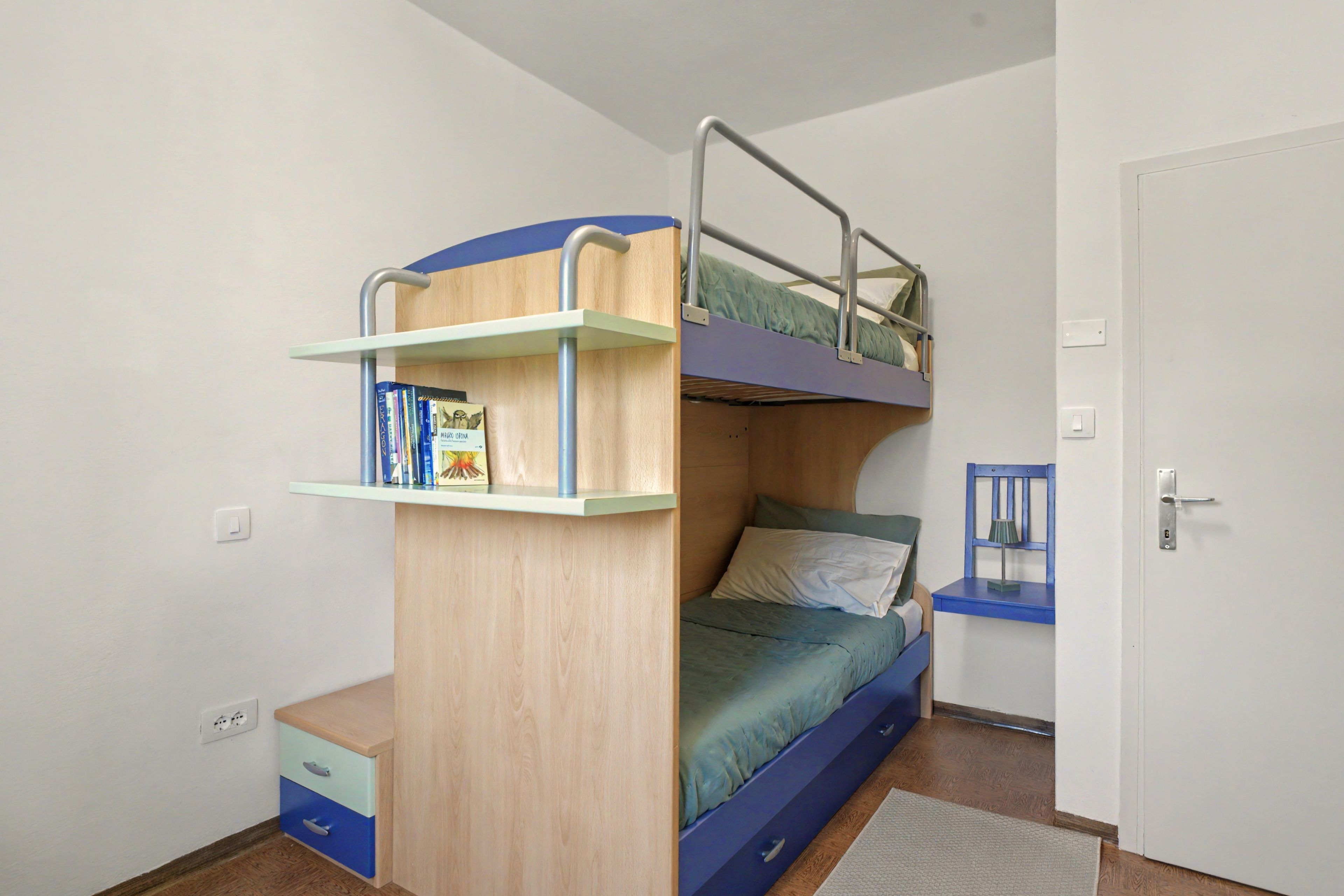 Una cama litera con estantería, una mesita de noche y una silla.