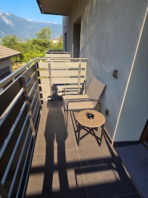 Ein Balkon mit Metallgeländer, einem Tisch mit Stühlen und Blick auf die Berge.