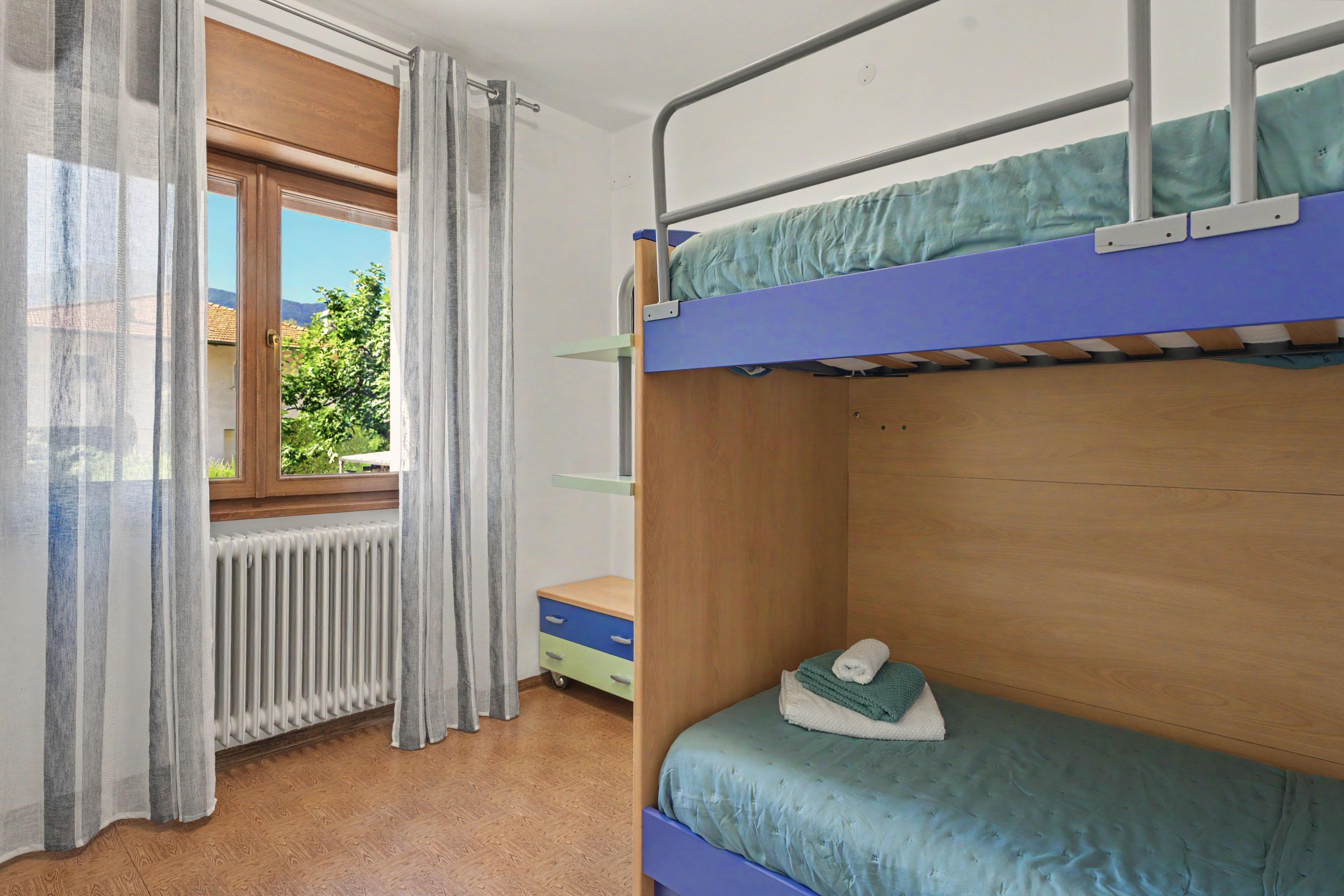 Ett rum med en våningssäng, ett fönster, ett element och ett litet bord.