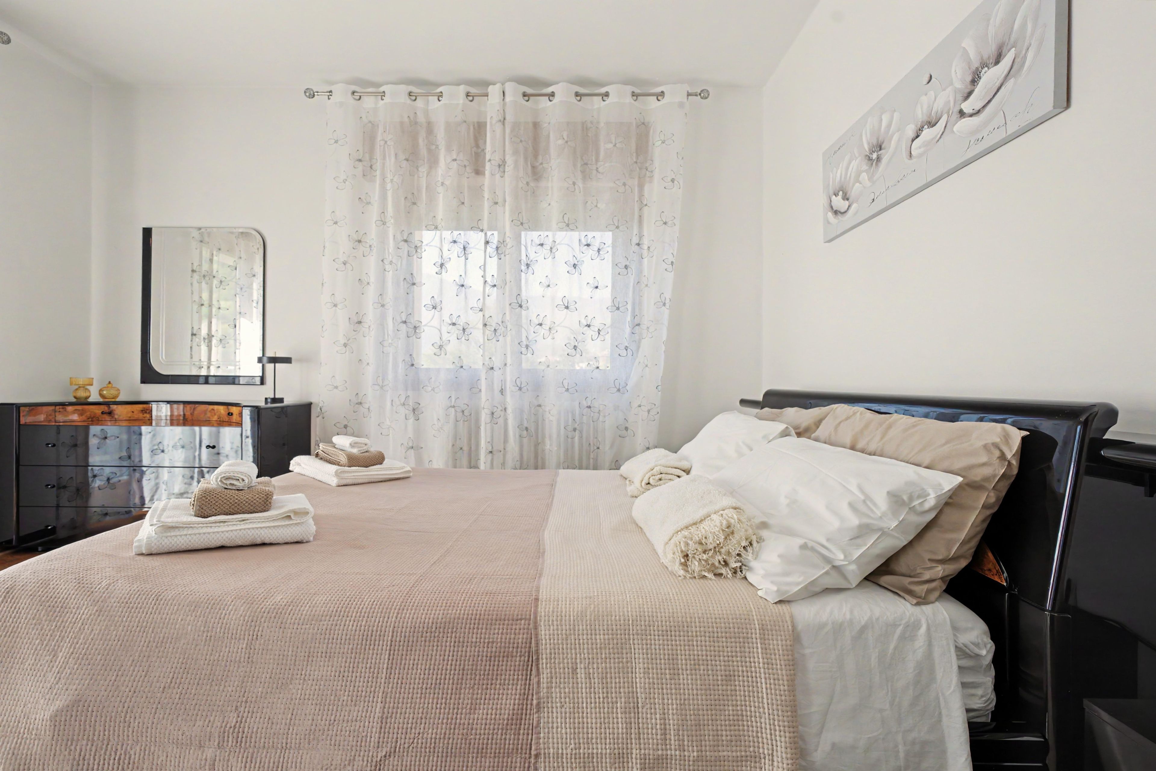 Une chambre à coucher avec un lit, une commode, un miroir et une fenêtre avec des rideaux.